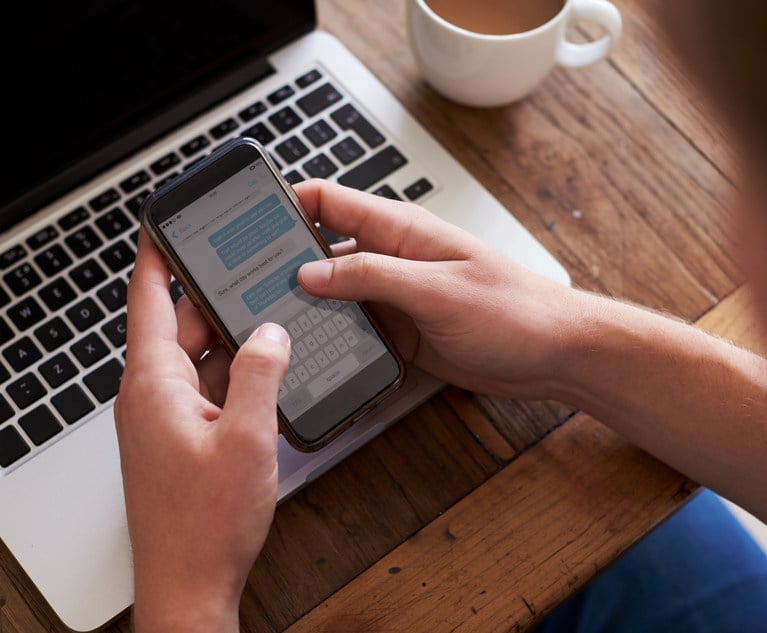 Man Sending Text Message On Mobile Phone Whilst Using Laptop