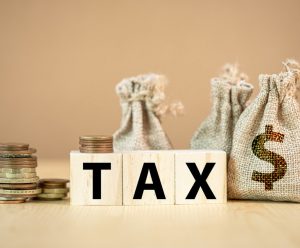 Tax wording on wooden cubes with US dollar coins and bag.