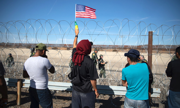 A Central American migrant holds an American flag in front of barbed wire along the U.S. and Mexico border in Tijuana, Mexico, on Nov. 25, 2018. Photographer: Tomas Ayuso/Bloomberg