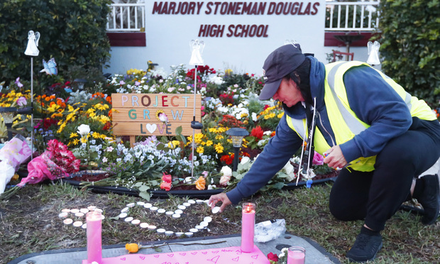 School crossing guard Wendy Behrend lights a candle at a memorial outside Marjory Stoneman Douglas High School during the one-year anniversary of the school shooting, Thursday, Feb. 14, 2019, in Parkland, Fla. A year ago on Thursday, 14 students and three staff members were killed when a gunman opened fire at the high school. 